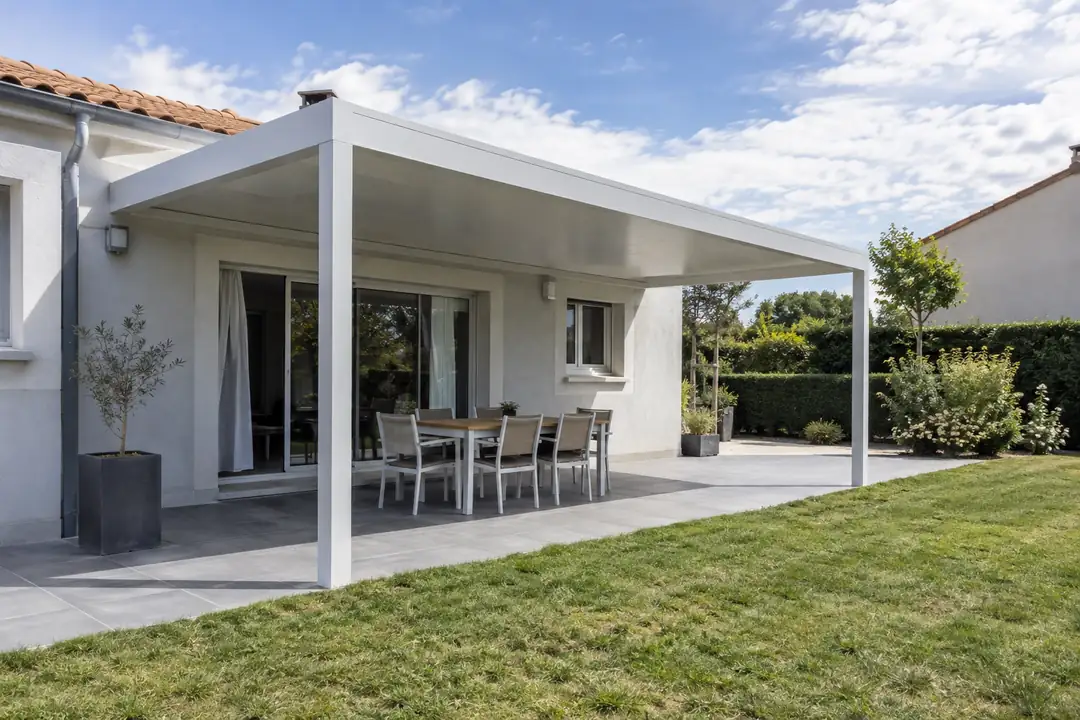 Pergola aluminium blanche à toit plein adossée à une maison récente, ouverte sur la pelouse